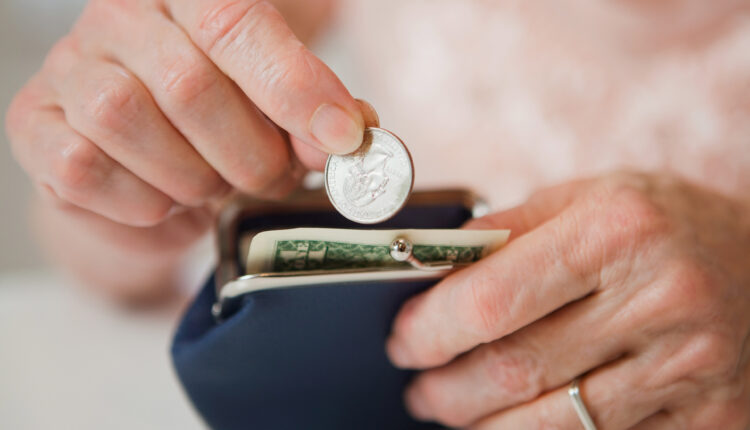 An up close photograph of the hands of a senior woman putting money into a coin purse.