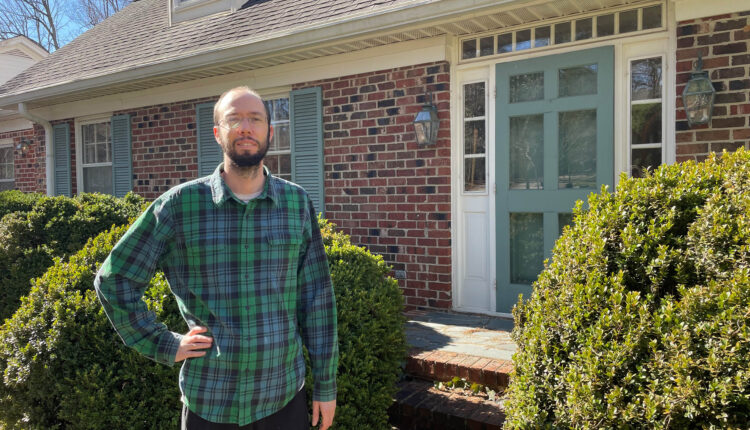 Patrick Dunnagan stands outside his North Carolina home on a sunny day. He wears a plaid shirt and glasses.