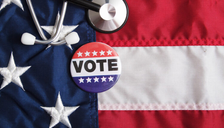 A stethoscope and voting pin rests on top of an American flag.