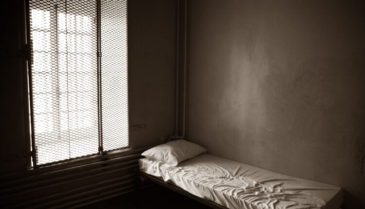 An empty prison cell with a bed in it.