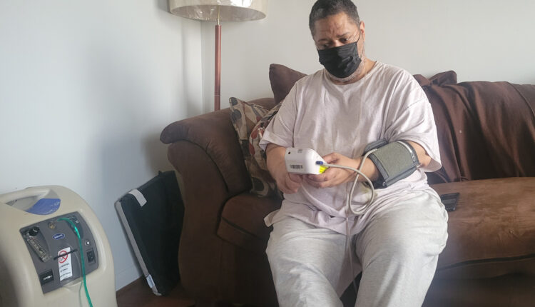 A man seated on his coach at home measures his blood pressure.