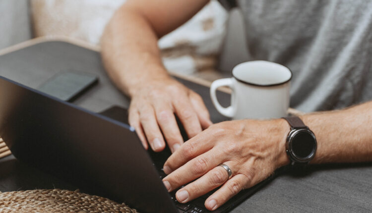 A close up photo of a man typing on a laptop.